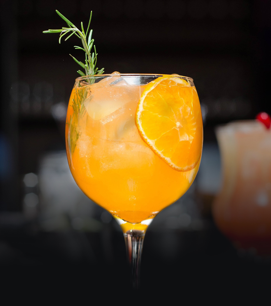 Hart an der Grenze Abendveranstaltungen Bild von einem alkohlältigen Spritzgetränk dekoriert mit einer Orangenscheibe vor dem Hintergrund einer Bar